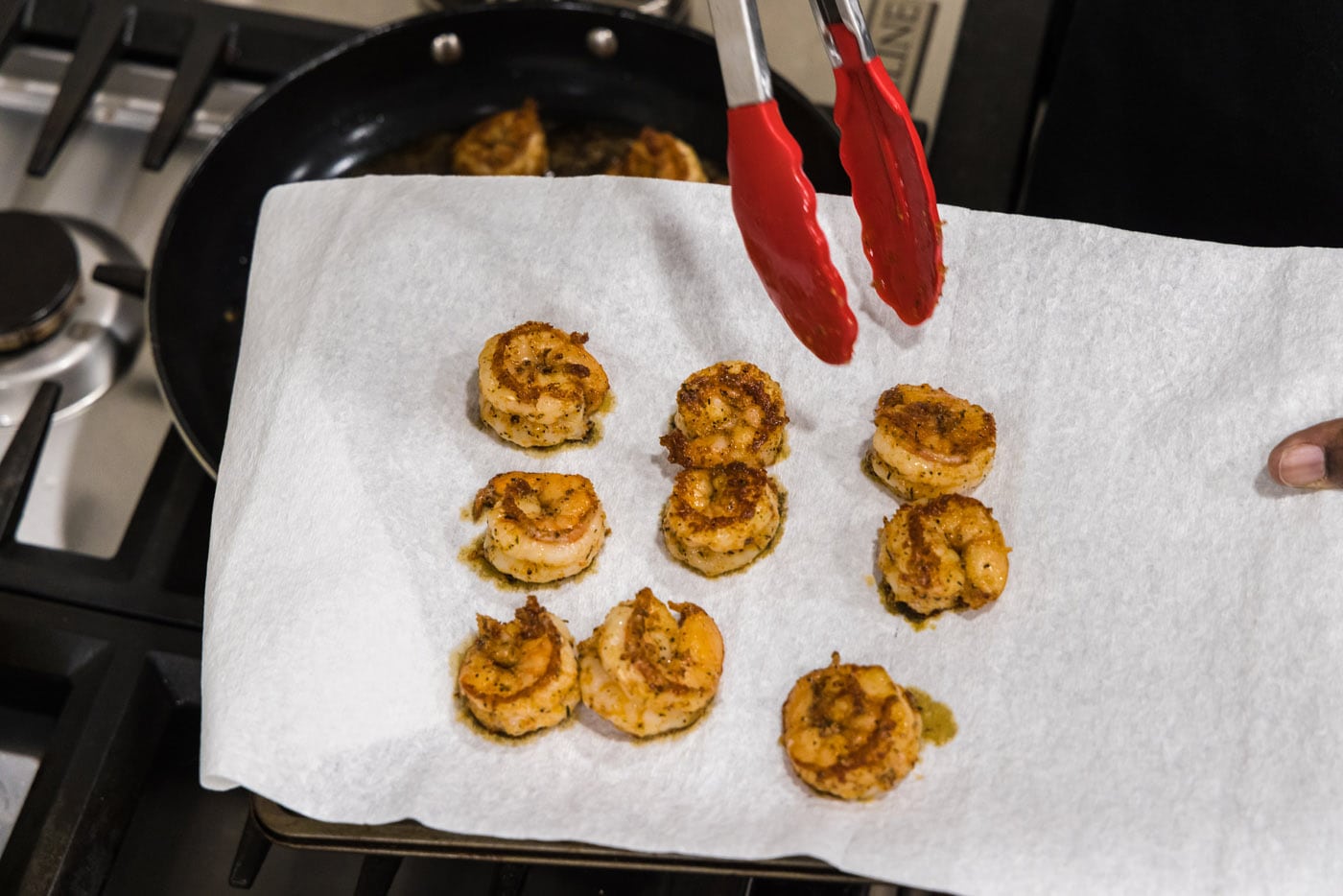 tongs moving cooked shrimp to a paper towel to drain