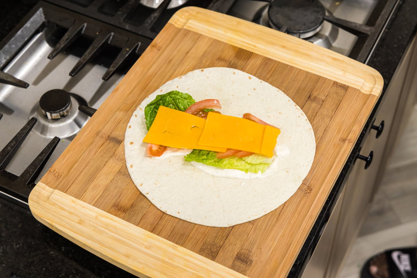 sliced cheese on top of lettuce, ranch, and tomato tortilla