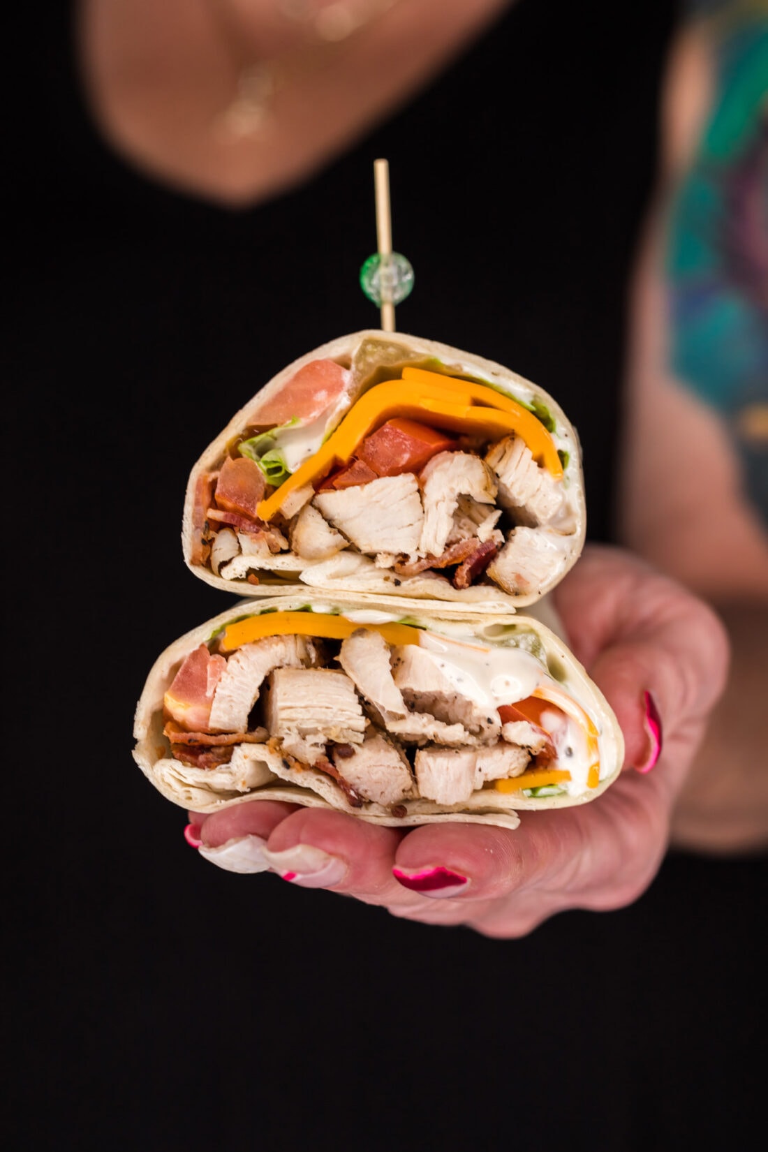 Hand holding two halves of a Chicken Bacon Ranch Wrap stacked on top of each other