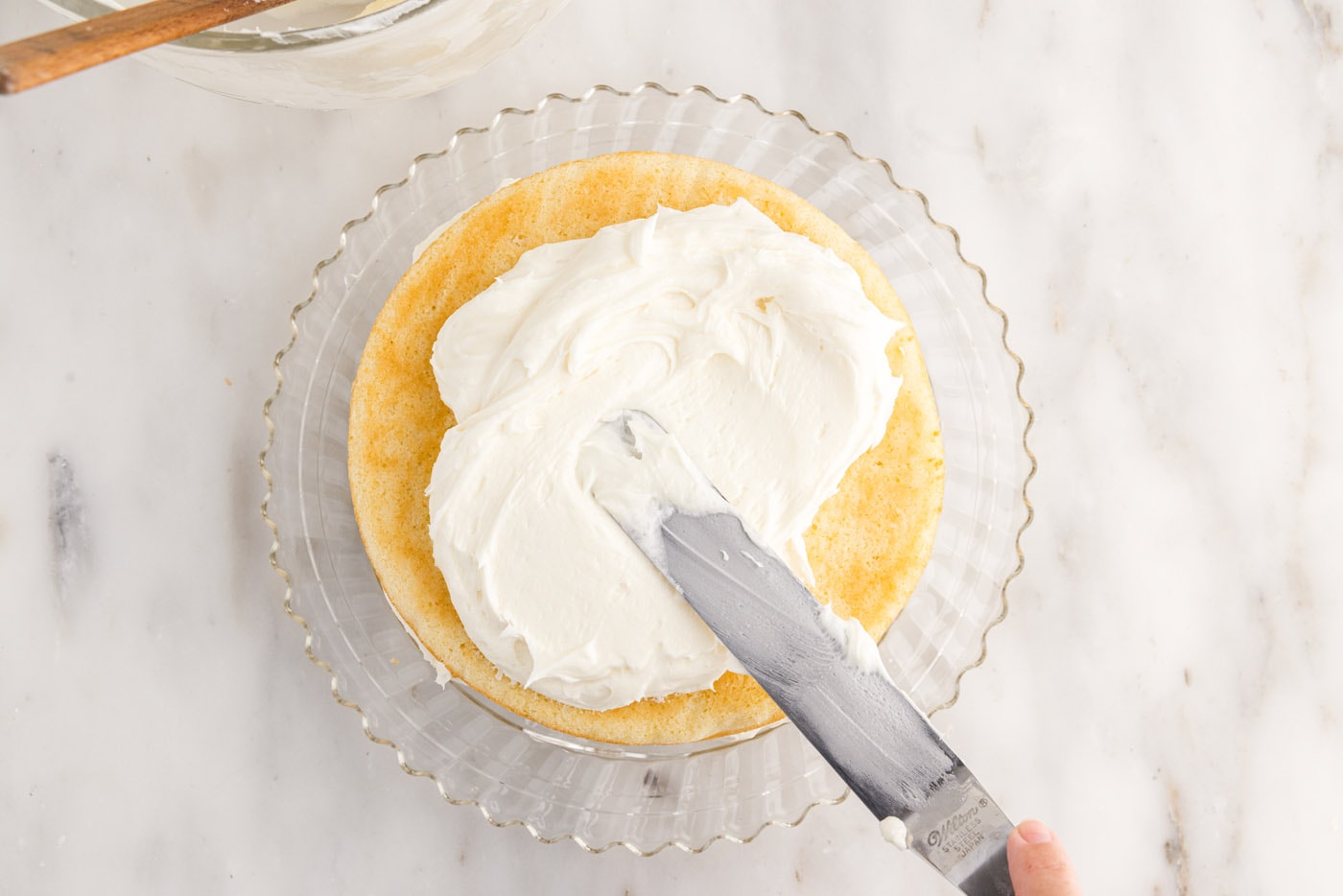 spreading cream cheese frosting on top of cake