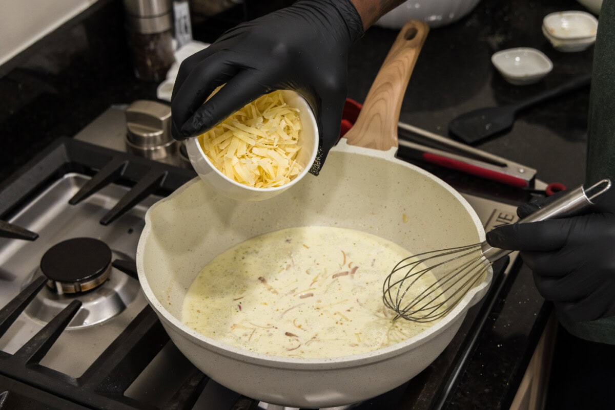 adding parmesan cheese to skillet with heavy cream