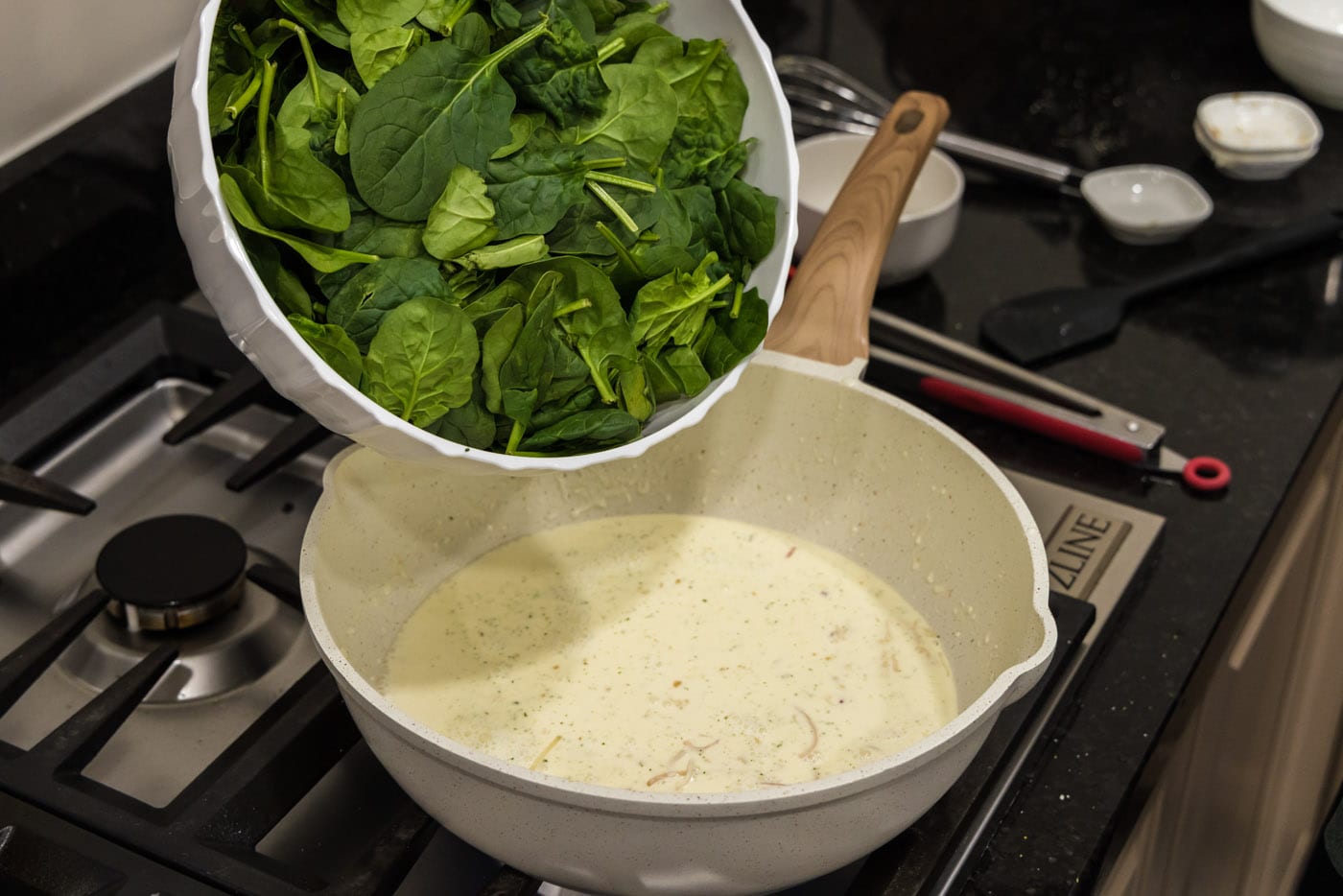 adding spinach to skillet with heavy cream mixture