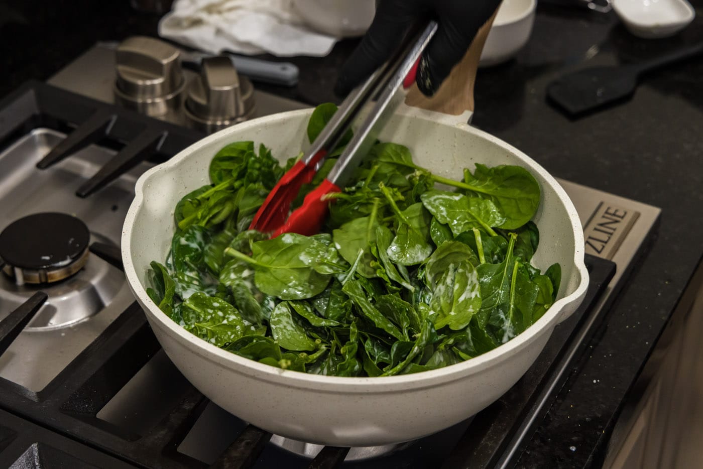 tongs tossing spinach in skillet