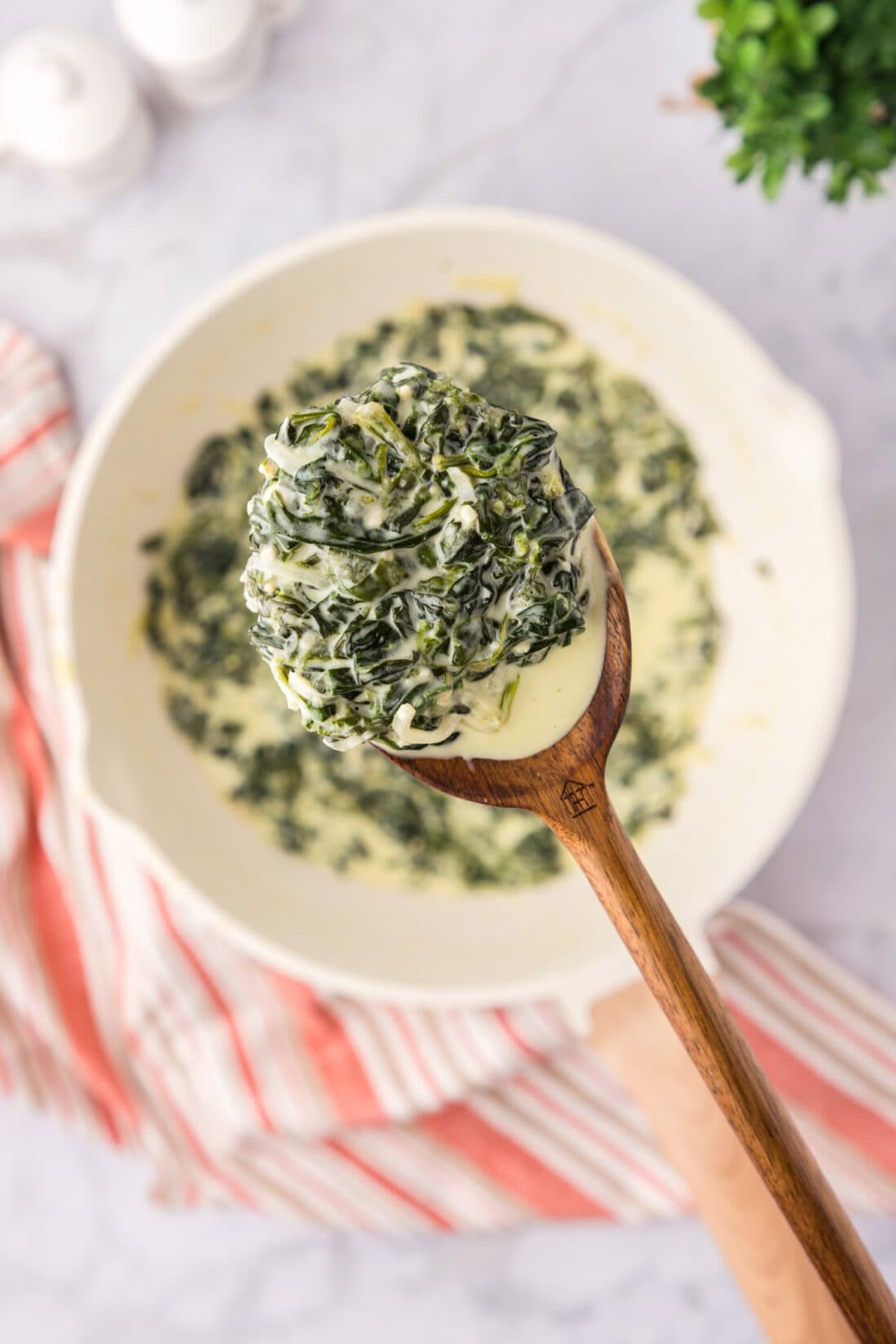 Spoonful of Creamed Spinach held above a skillet of Creamed Spinach