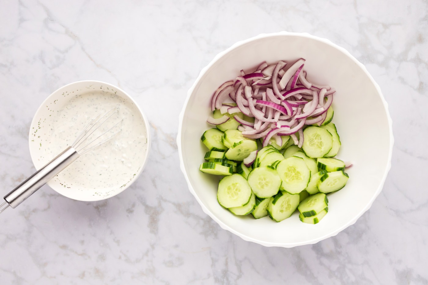 red onion and cucumber in a mixing bowl along with creamy dressing on the side