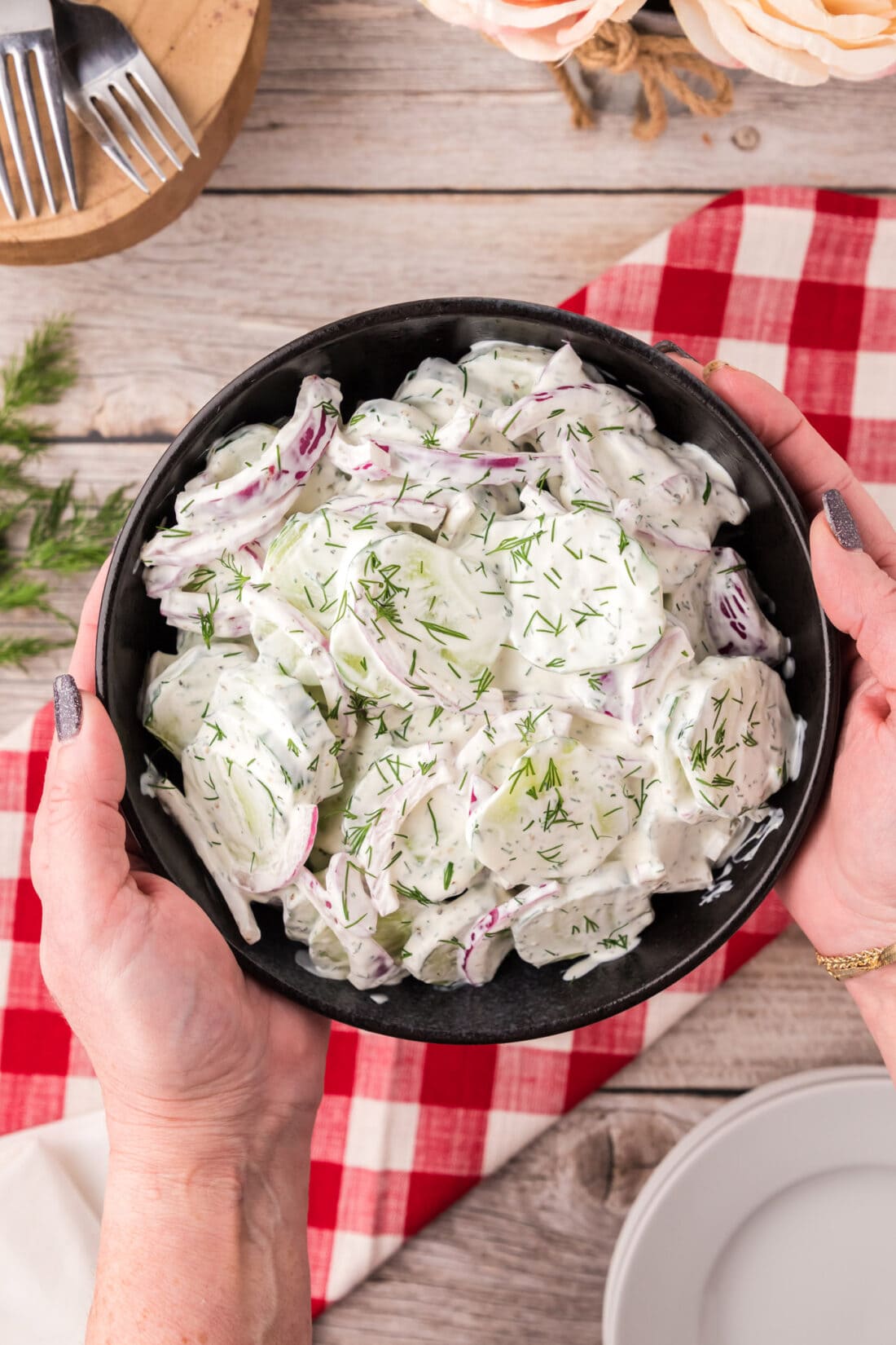 Hands holding a bowl of Creamy Cucumber Salad