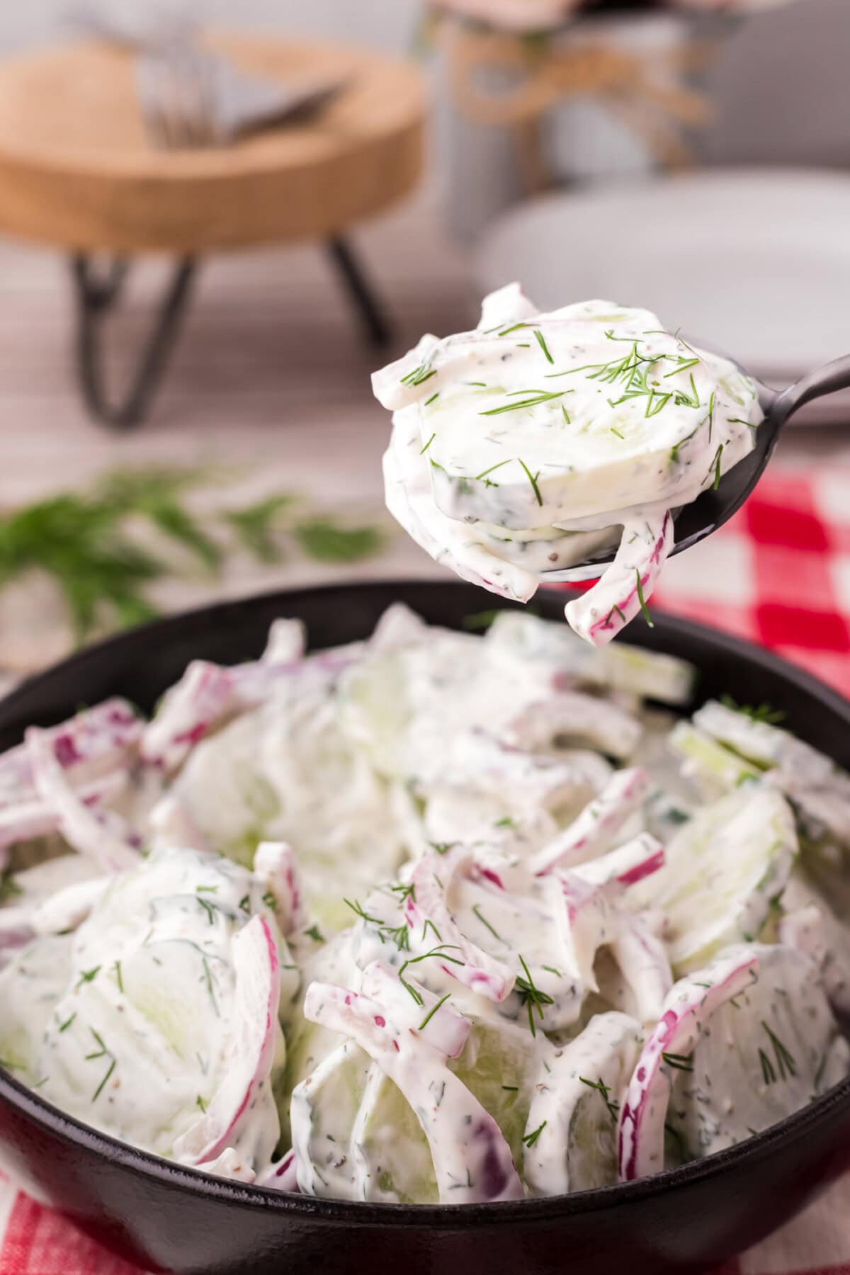 Spoonful of Creamy Cucumber Salad held above a bowl of Creamy Cucumber Salad
