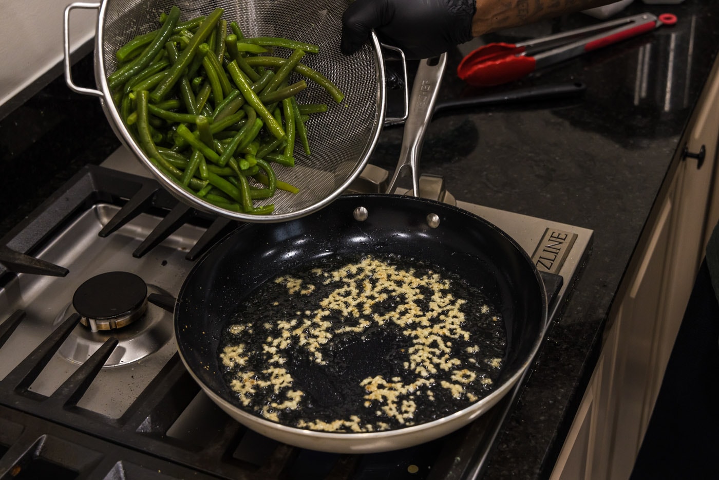 adding green beans to skillet with oil and garlic