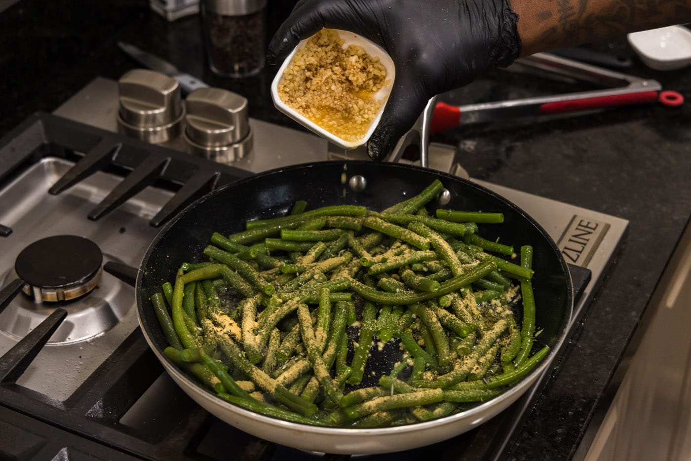 adding minced garlic to skillet with herbs and green beans