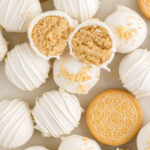 Close up photo of a Golden Oreo Truffle cut in half resting on top of more Golden Oreo Truffles