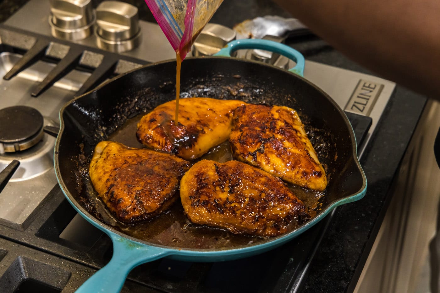 pouring marinade into skillet with chicken breasts