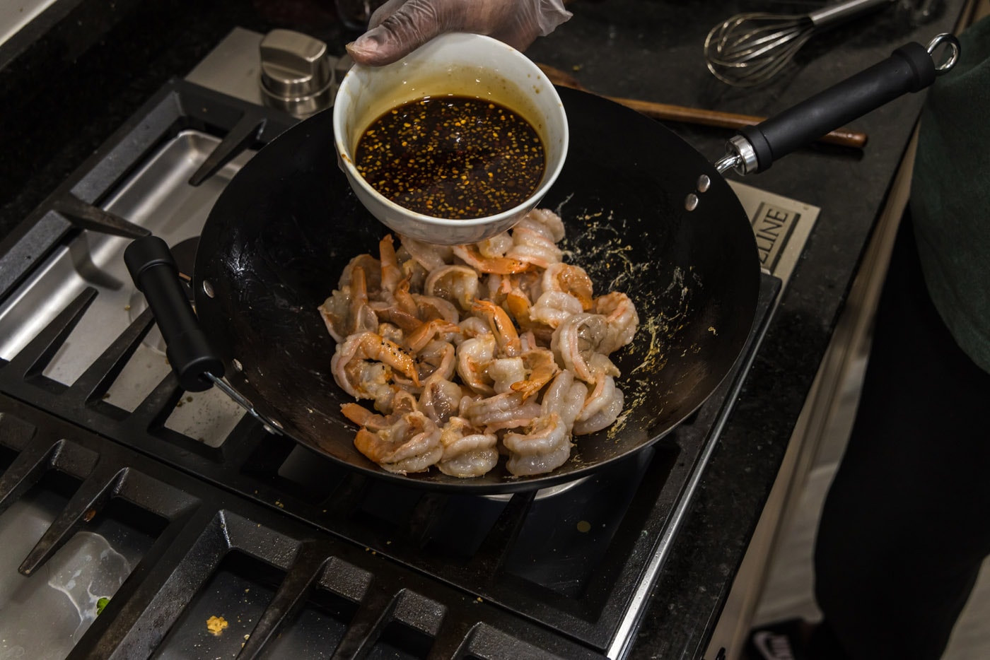 adding hunan sauce to shrimp in wok