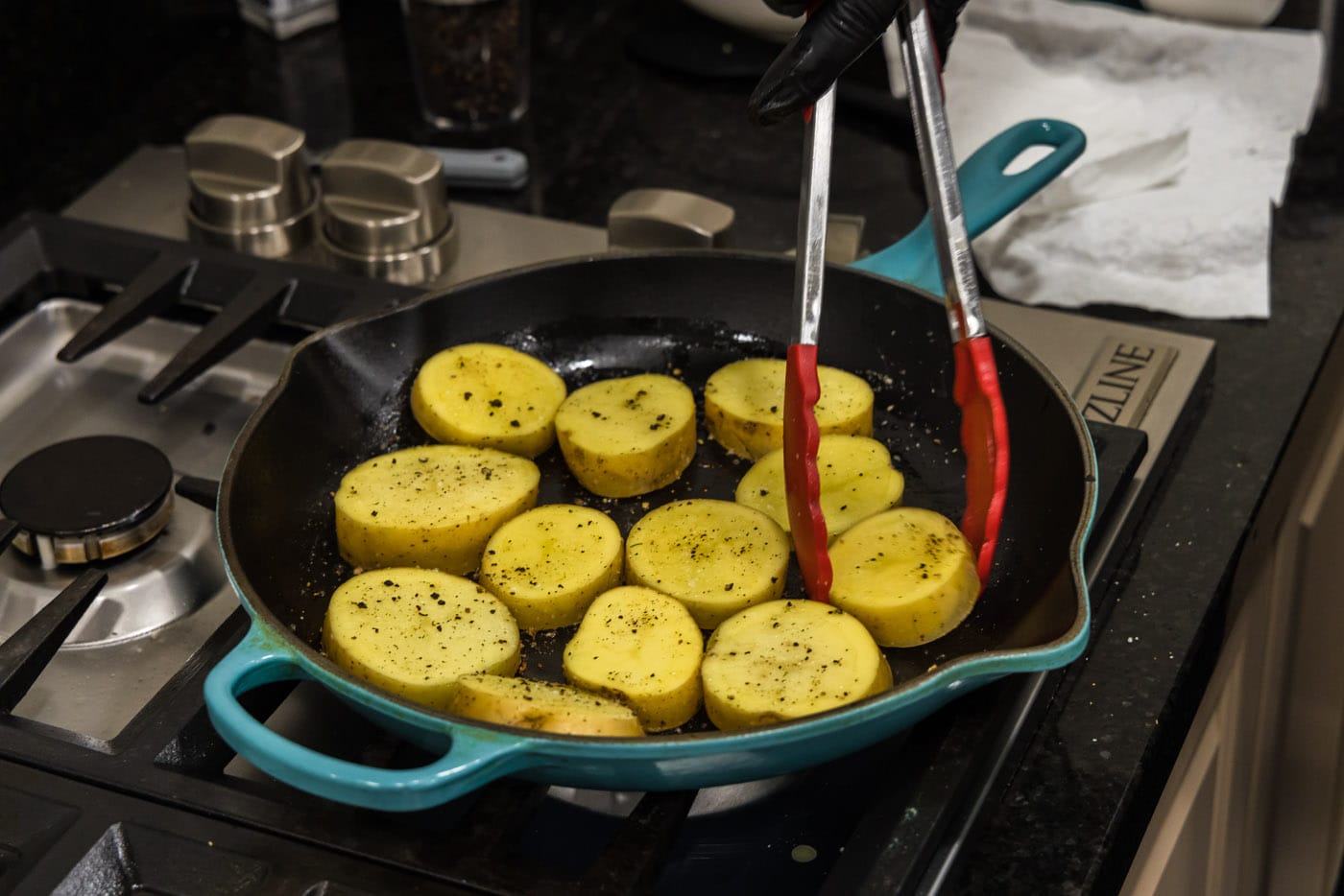 tongs turning over potato rounds in a skillet