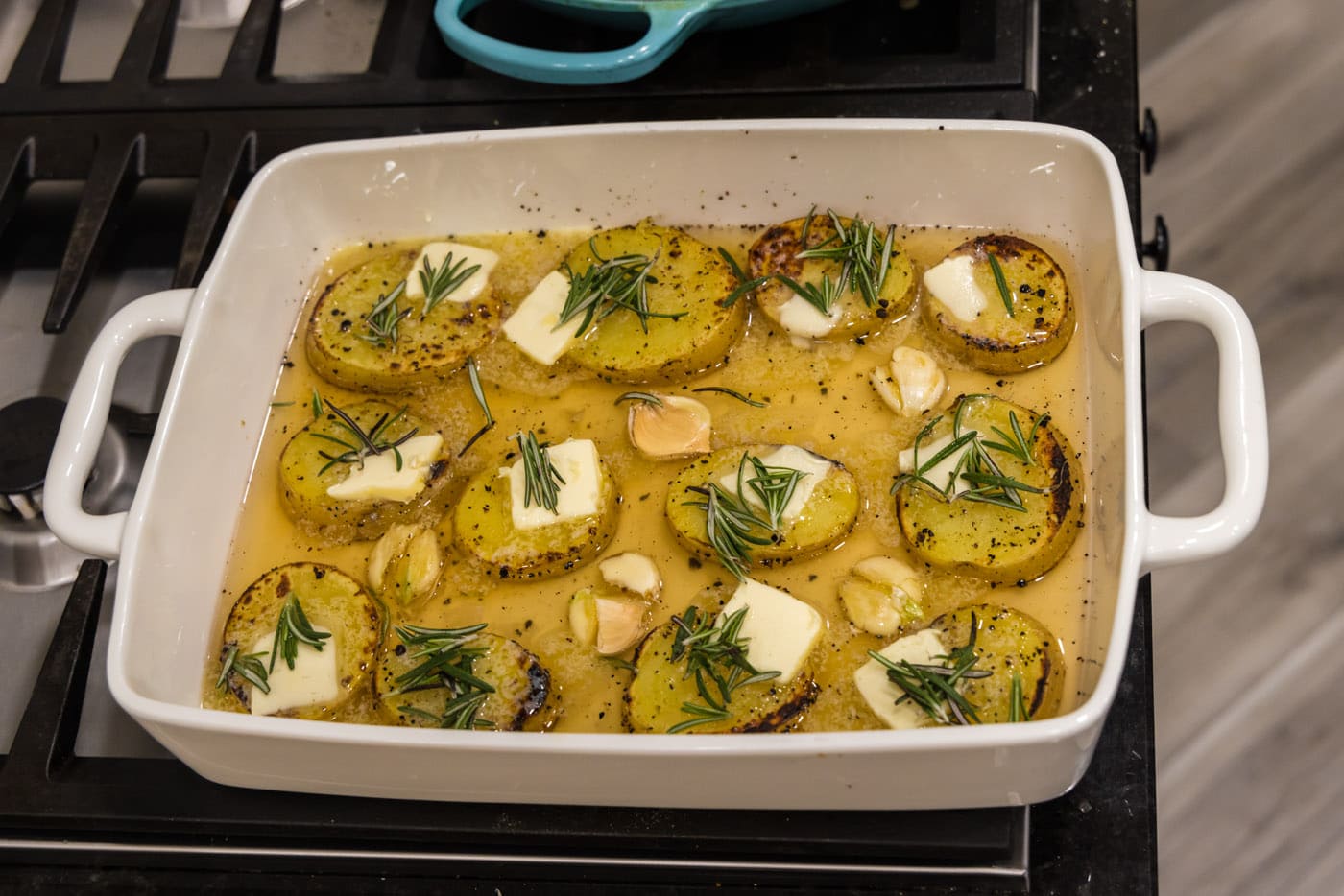potato slices in a baking dish with chicken broth, rosemary, and garlic