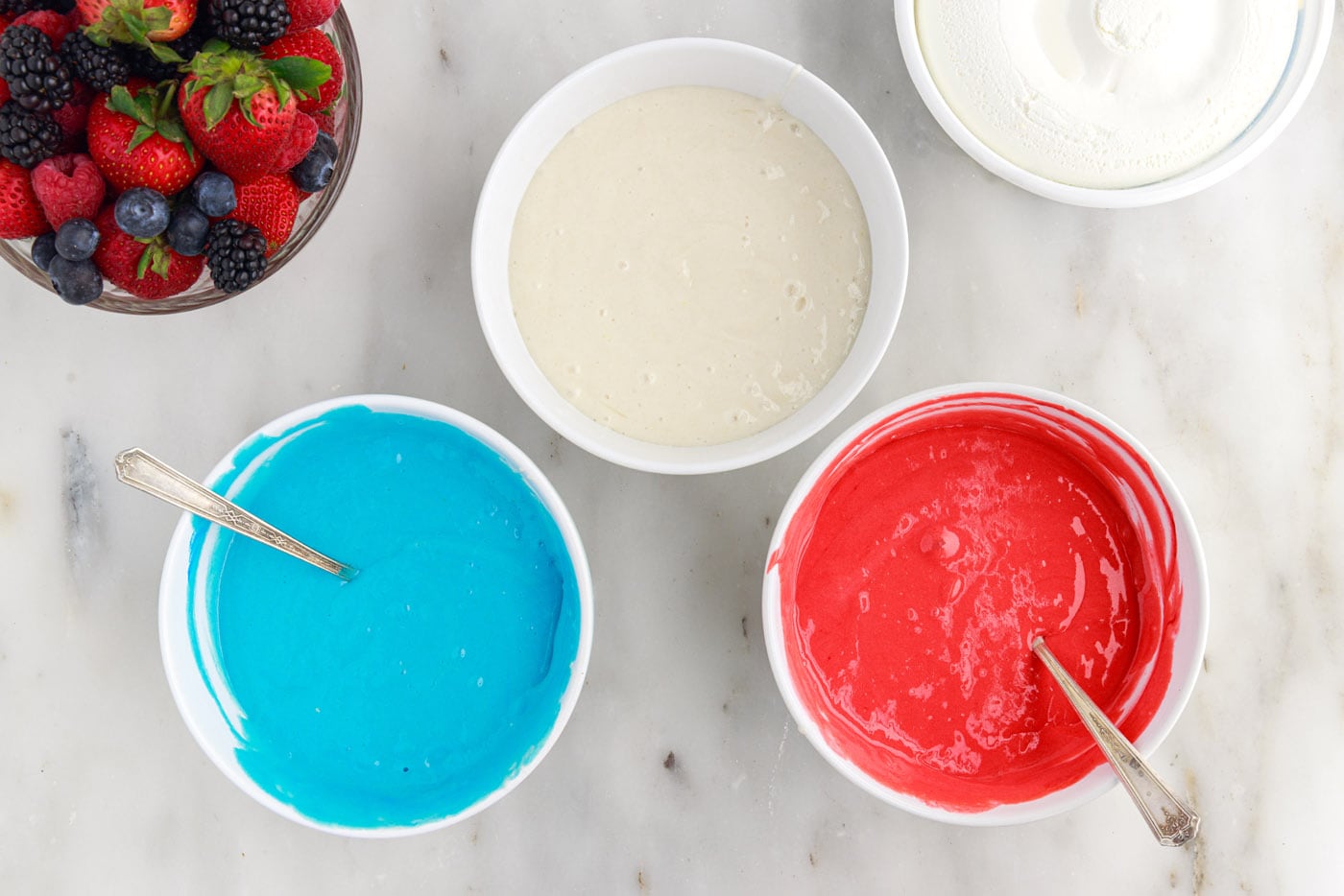 Red, white, and blue cake batter in bowls