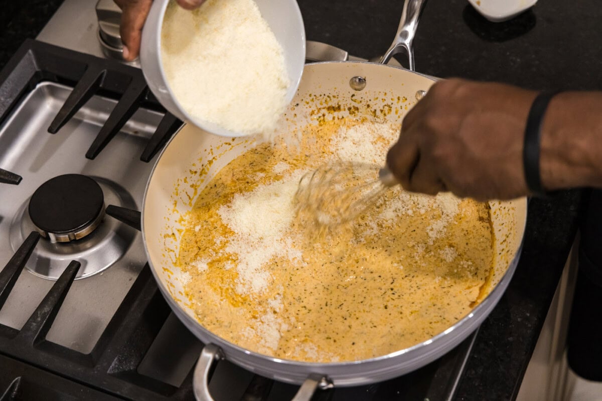 sprinkling parmesan cheese into skillet of alfredo saue