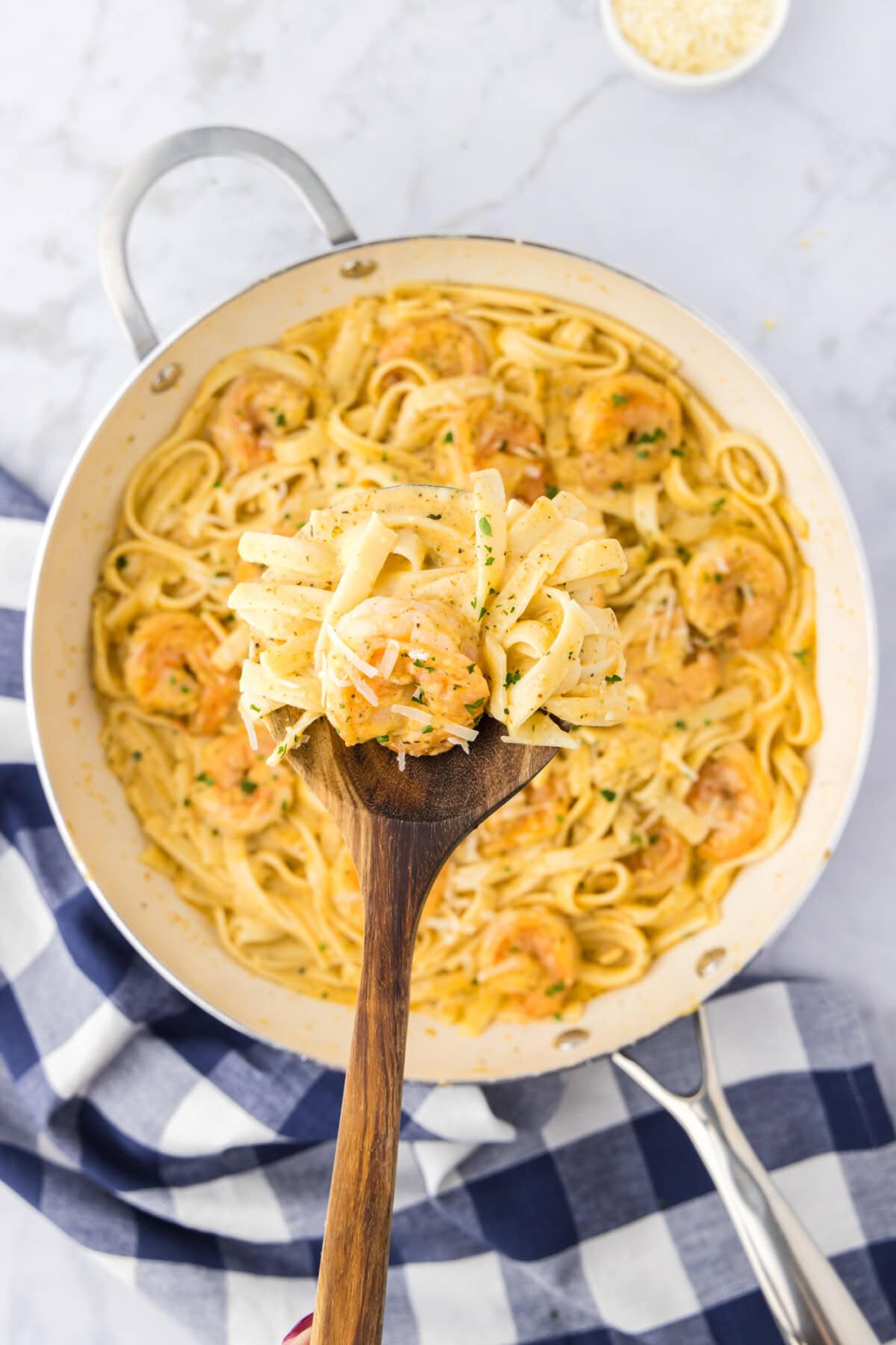 Spoonful of Shrimp Alfredo held above a skillet of Shrimp Alfredo