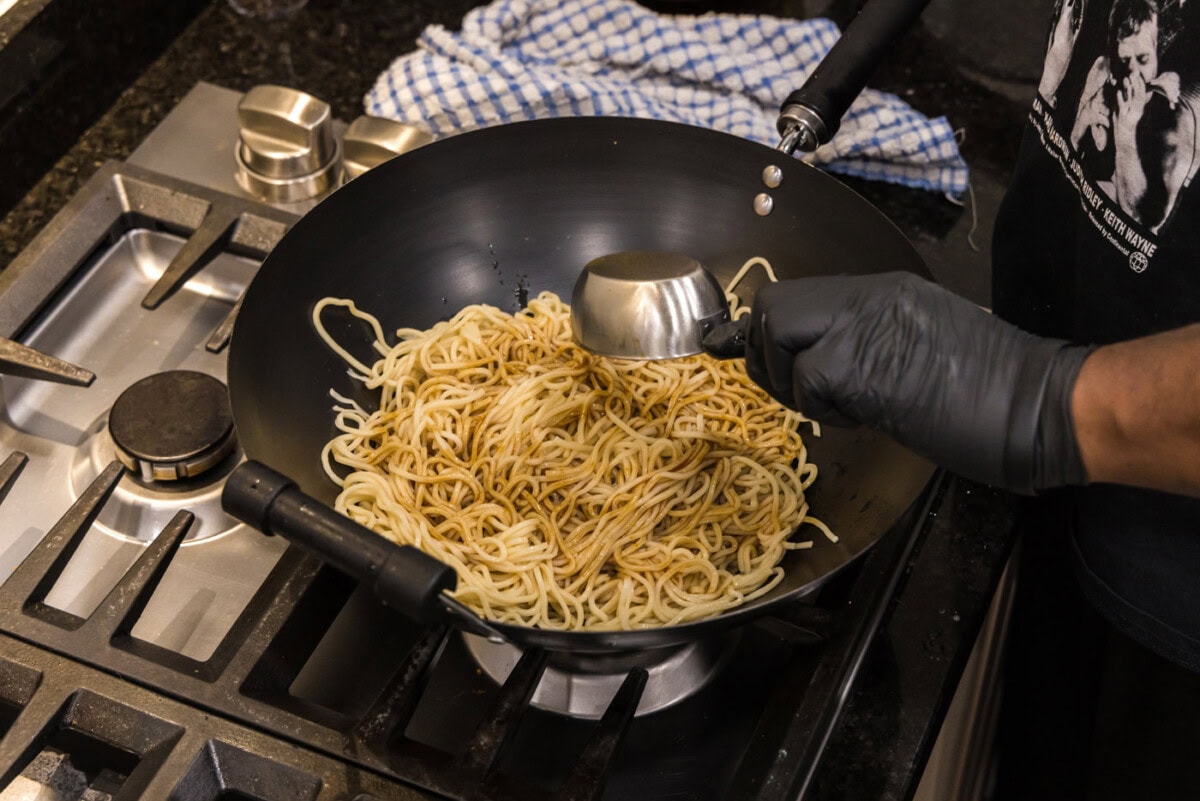adding teriyaki sauce to lo mein noodles in a wok