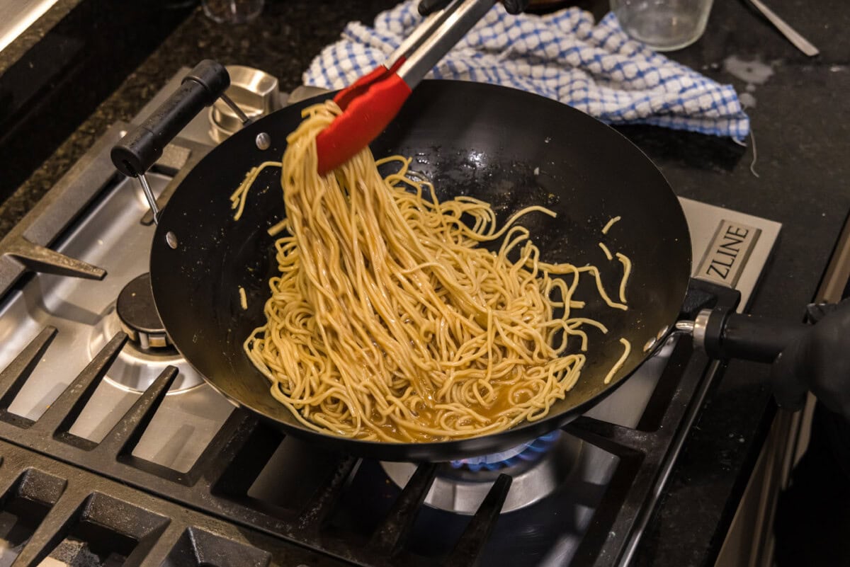 tongs picking up teriyaki noodles in a wok