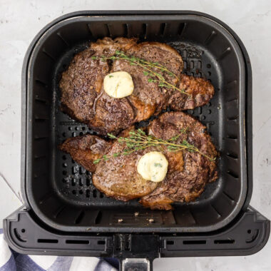 Two Air Fryer Steaks in an Air Fryer topped with butter