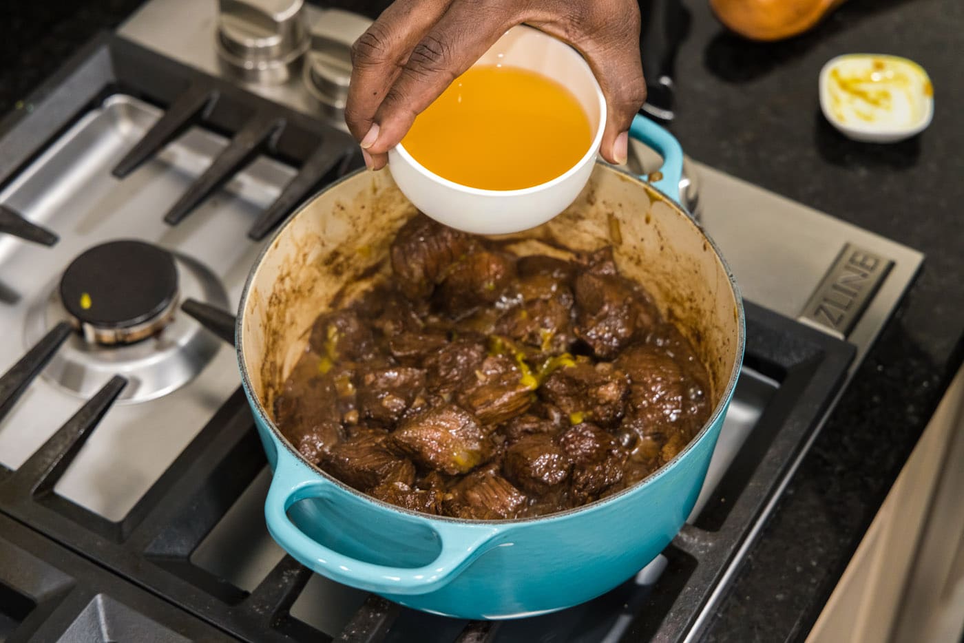 adding chicken stock to beef tips in a pot