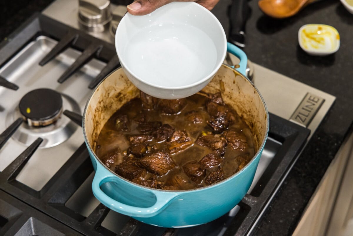 adding water to pot with cubed chuck roast