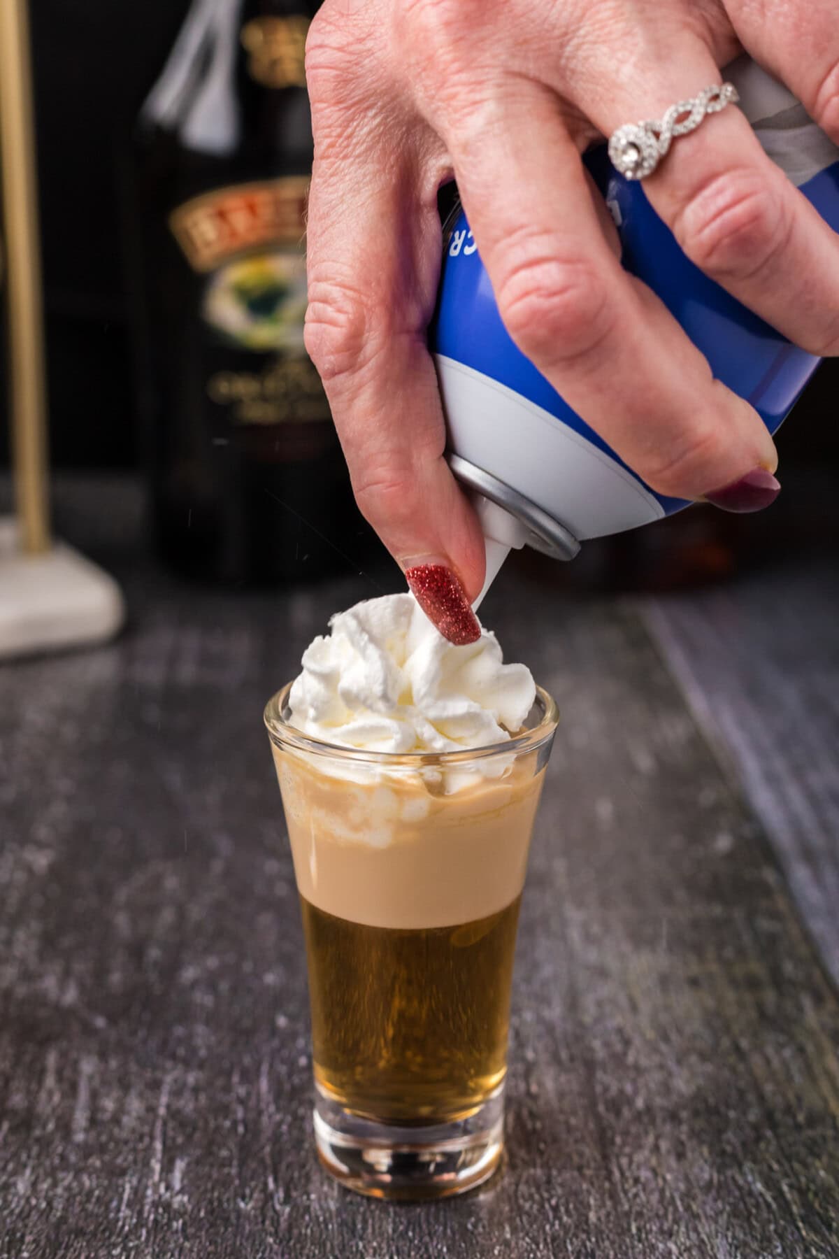adding whipped cream over buttery nipple shot