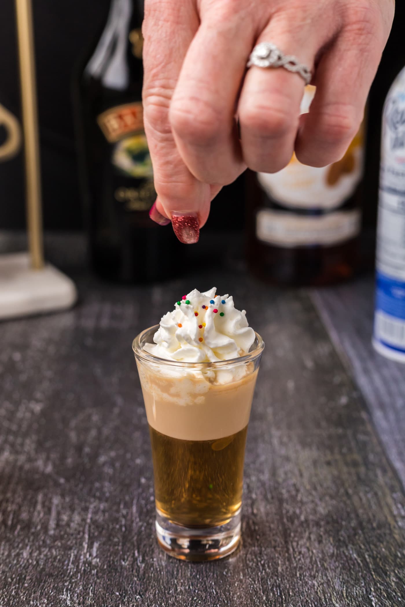adding sprinkles on top of whipped cream garnish on buttery nipple shot