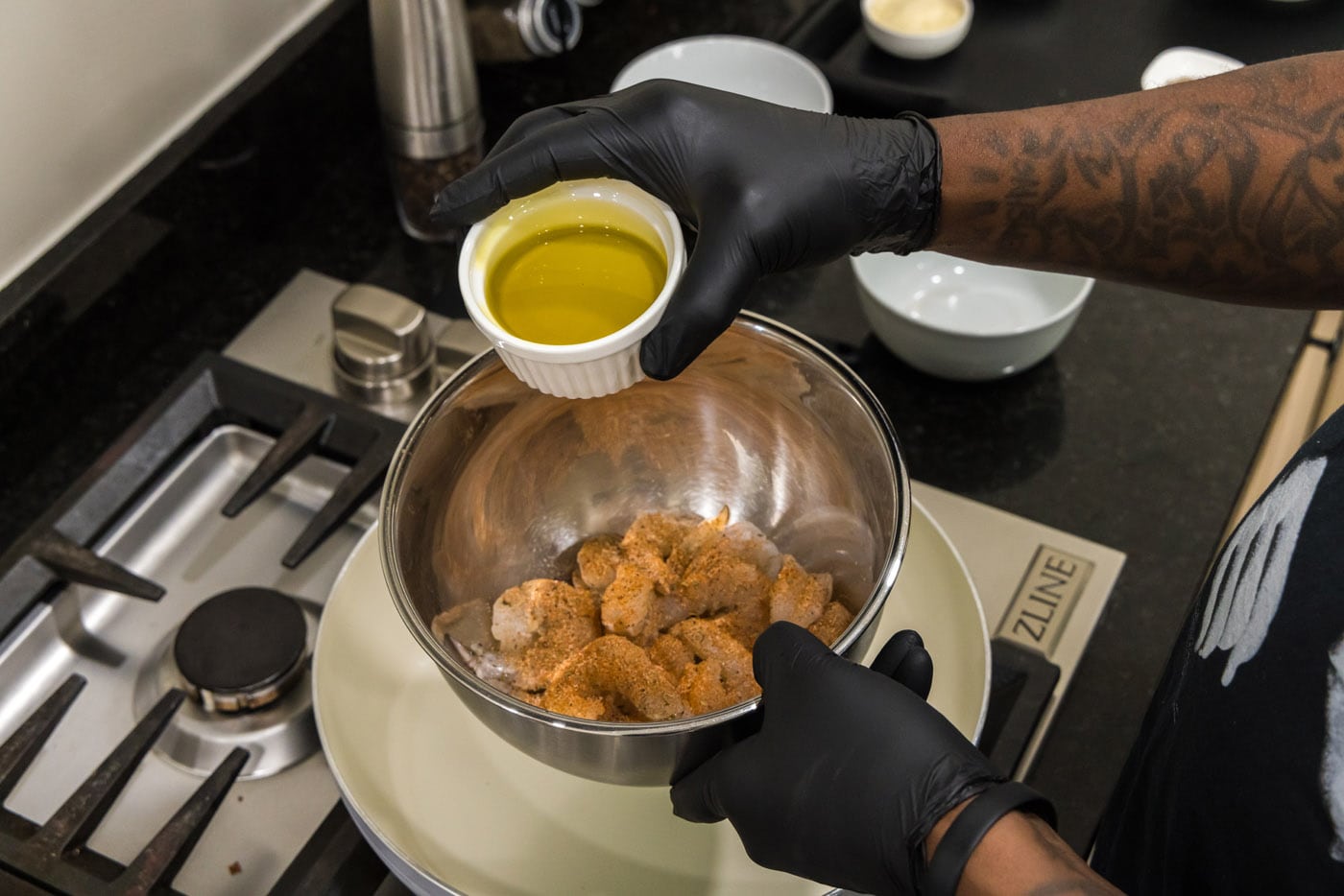 adding olive oil to seasoning shrimp in a bowl