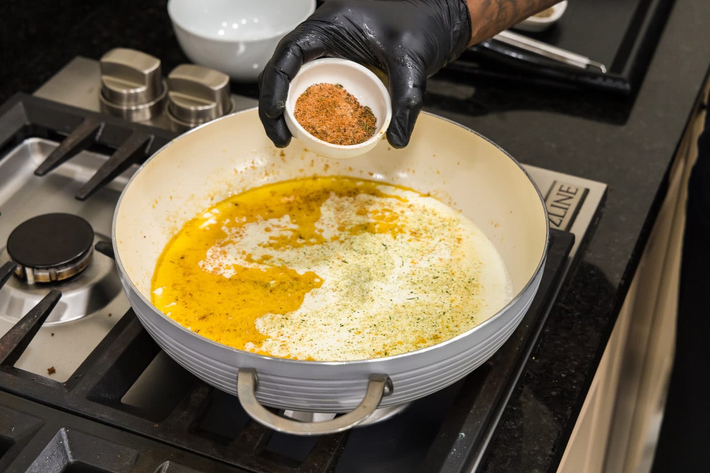 adding cajun seasoning to cream sauce in skillet