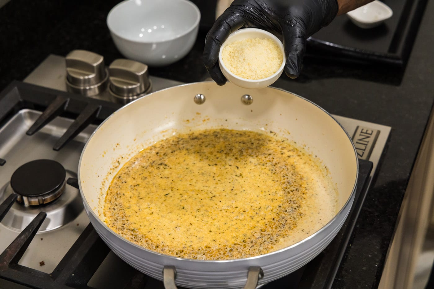 adding parmesan to cream sauce on the stovetop