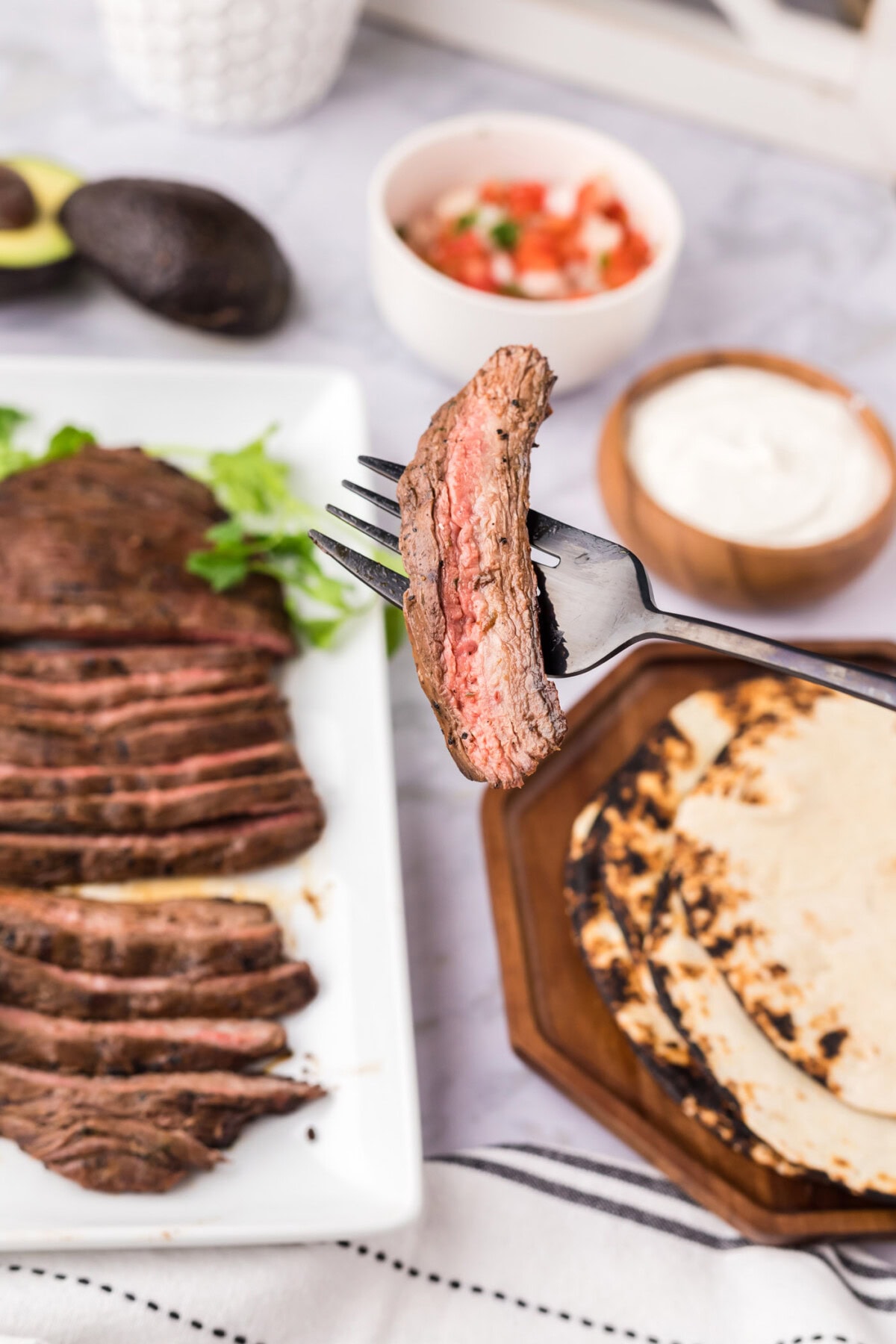Piece of Carne Asada on a fork with carne asada in the background and other toppings