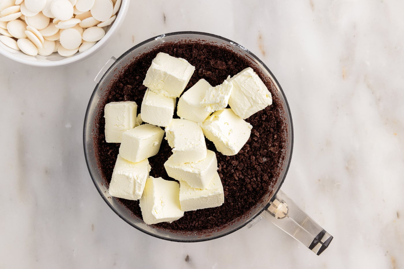 adding cream cheese cubes to food processor with oreos