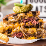 Patty Melt cut in half stacked on top of each other topped with a pickle