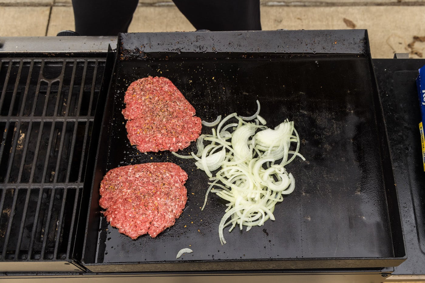 sliced onions cooking next to burger patties on a grill