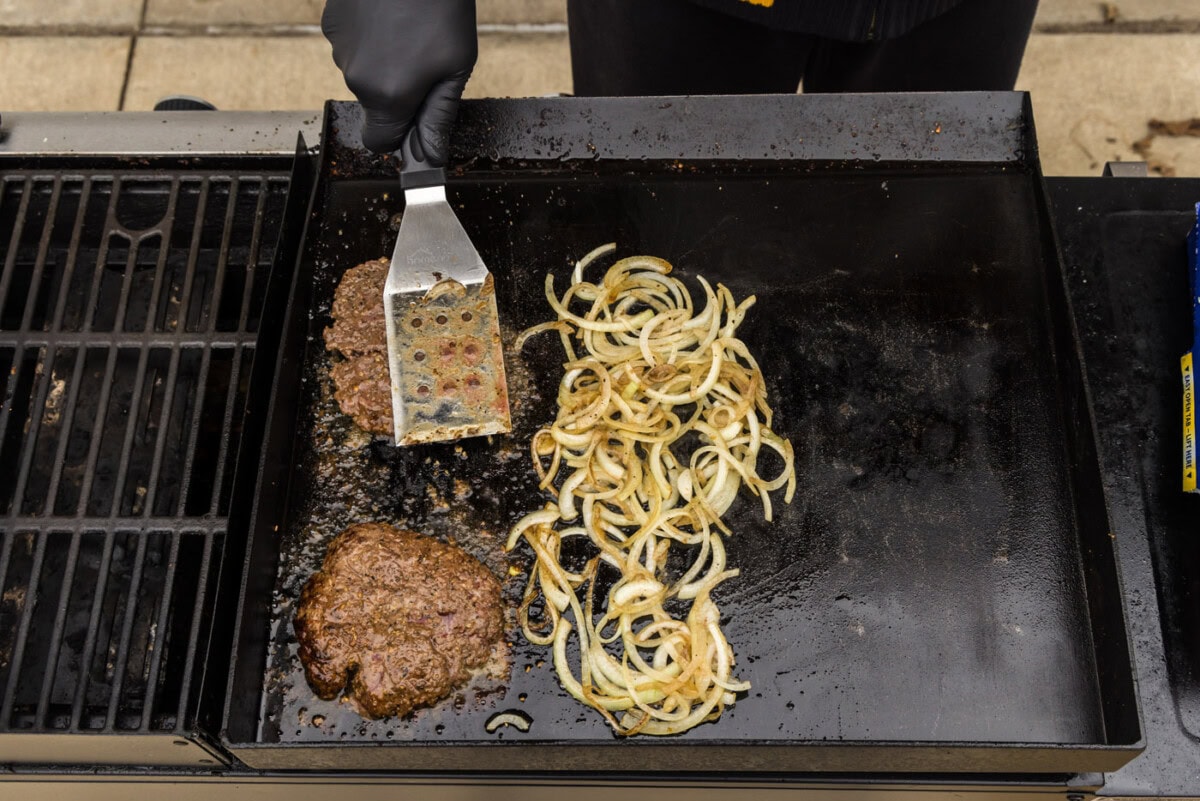 cooked burger patties with caramellized onions on a grill