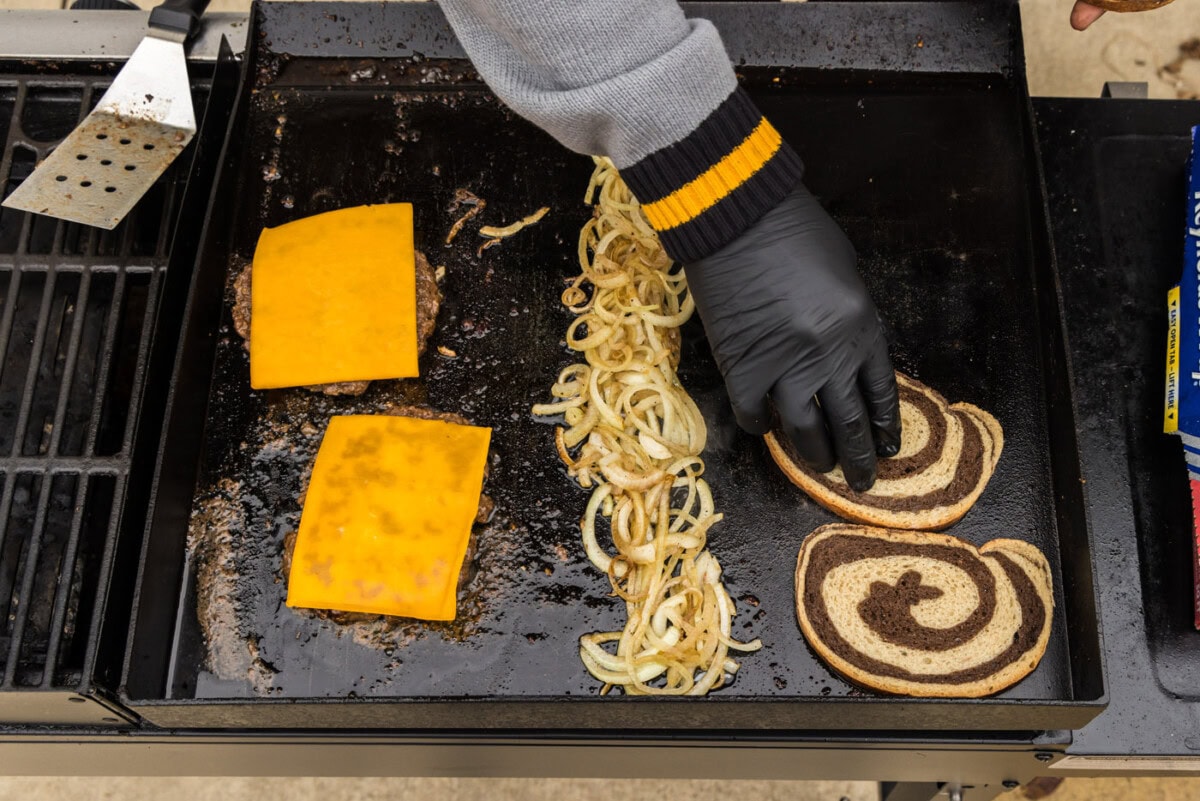adding rye bread to grill with onions and burger patties