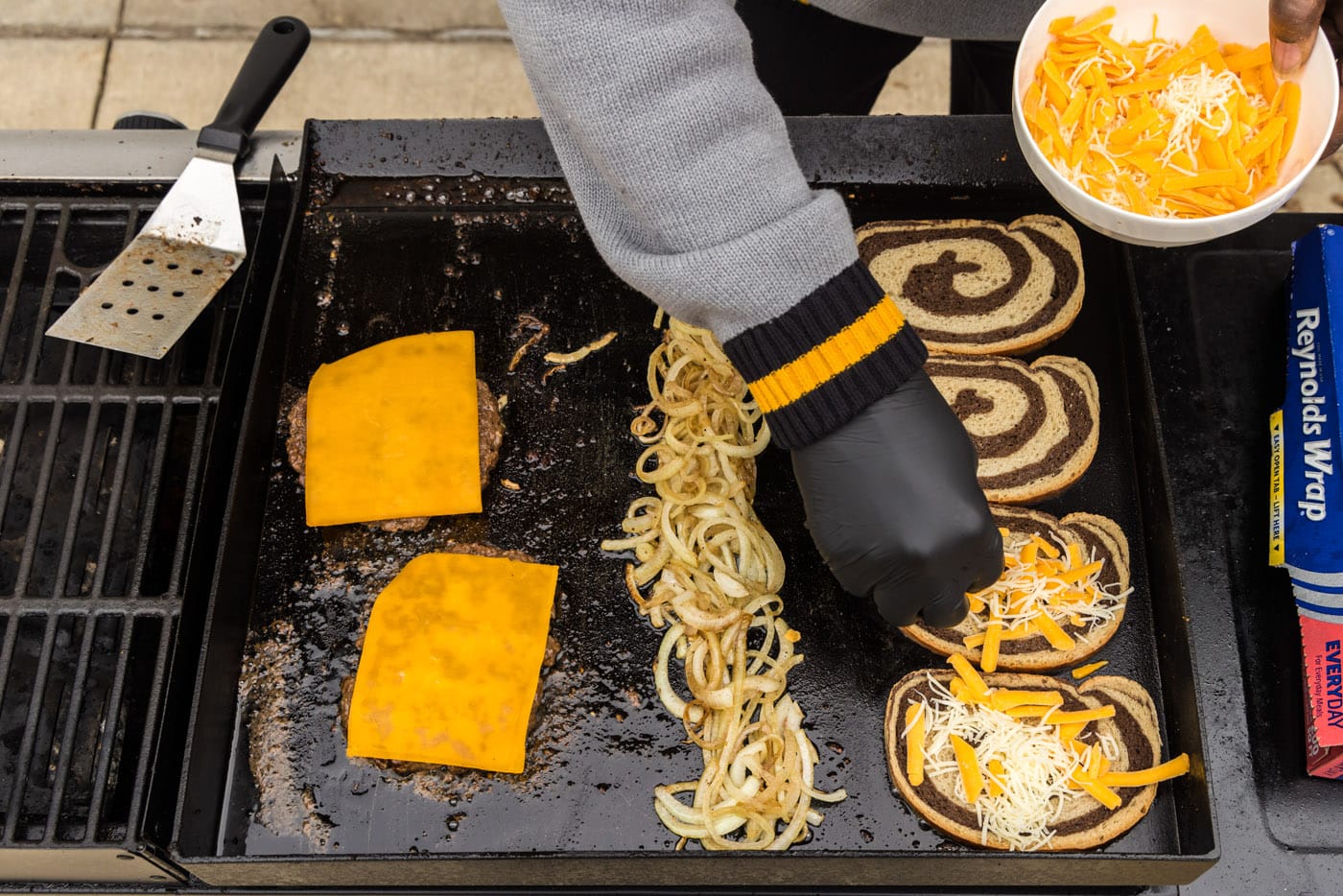 adding cheese to rye bread on a grill with onions and burgers