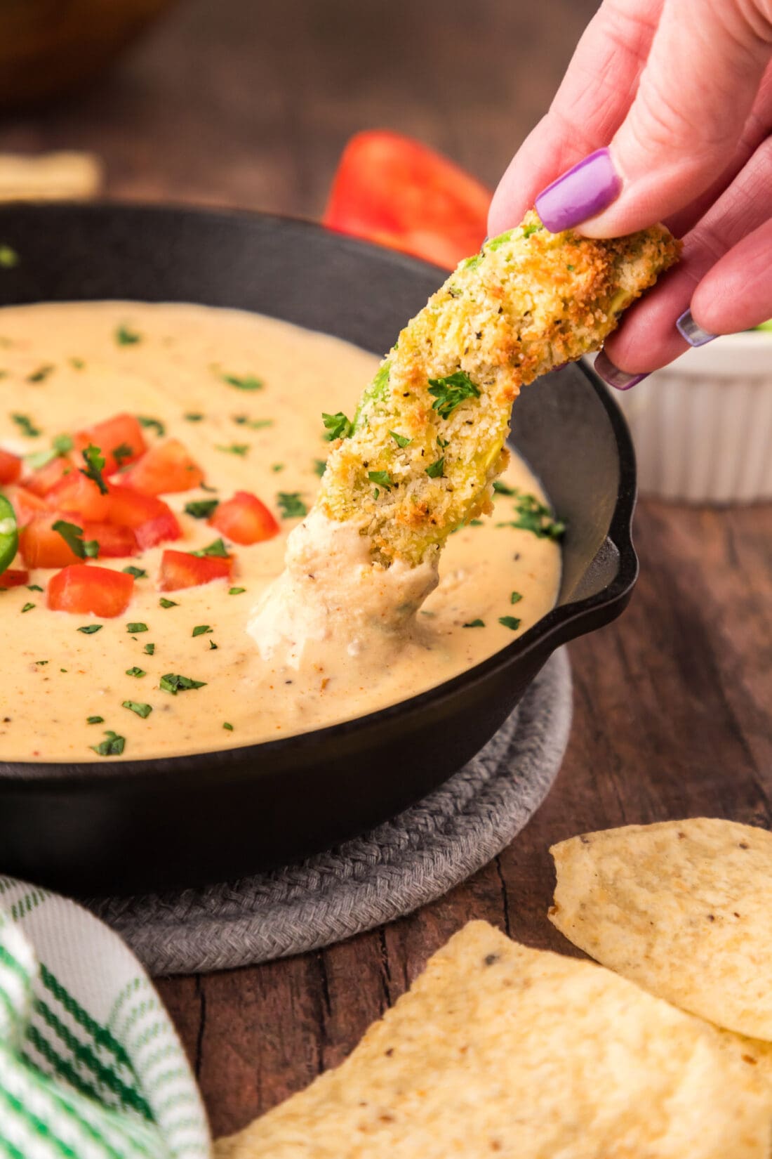 An air fryer avocado fry being dipped into a skillet of Queso Dip