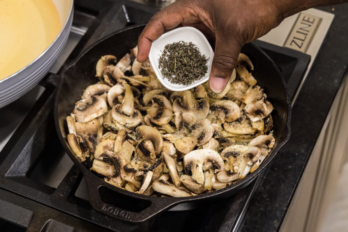 adding thyme leaves to skillet with mushrooms