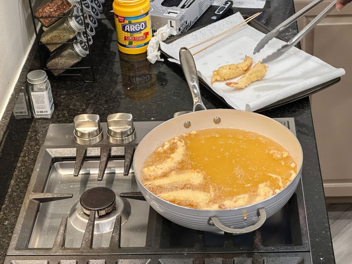 removing fried shrimp tempura from skillet with tongs