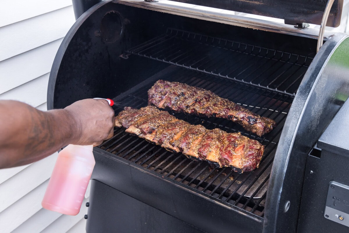 spraying beef ribs with apple cider vinegar mix on the smoker