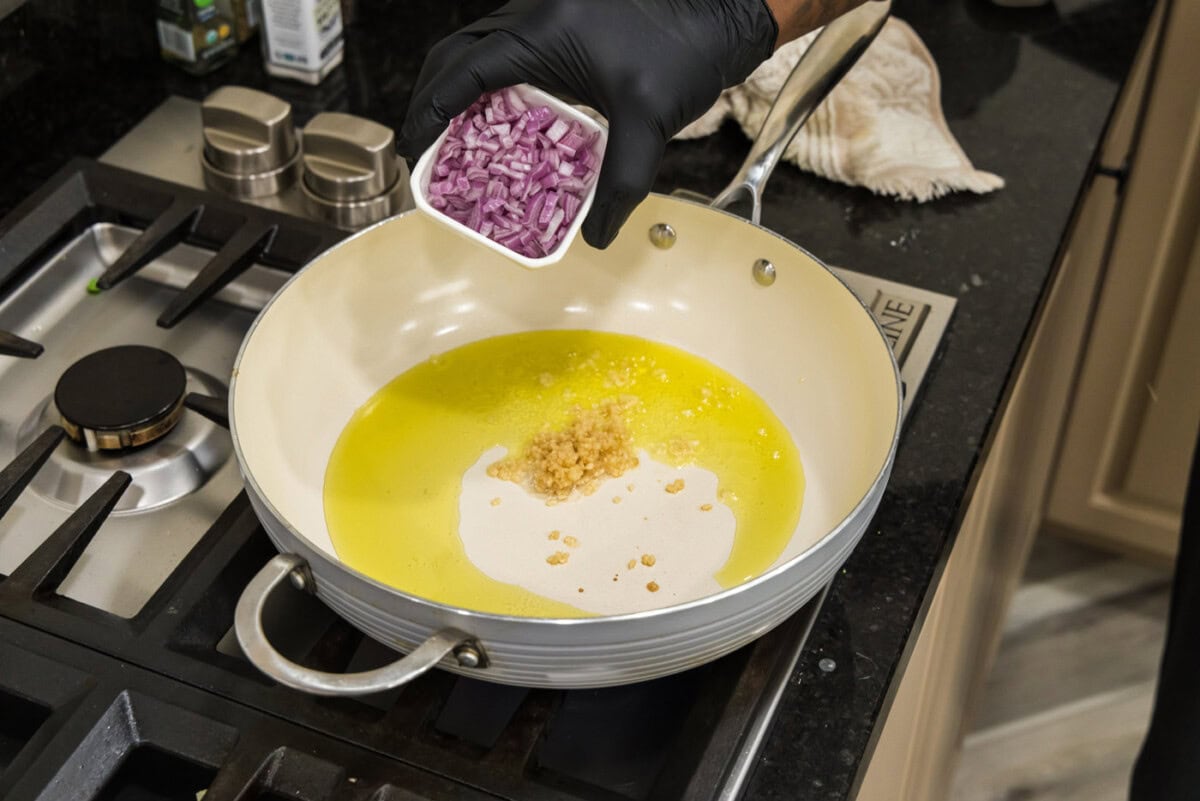 adding shallots to pan with oil and garlic