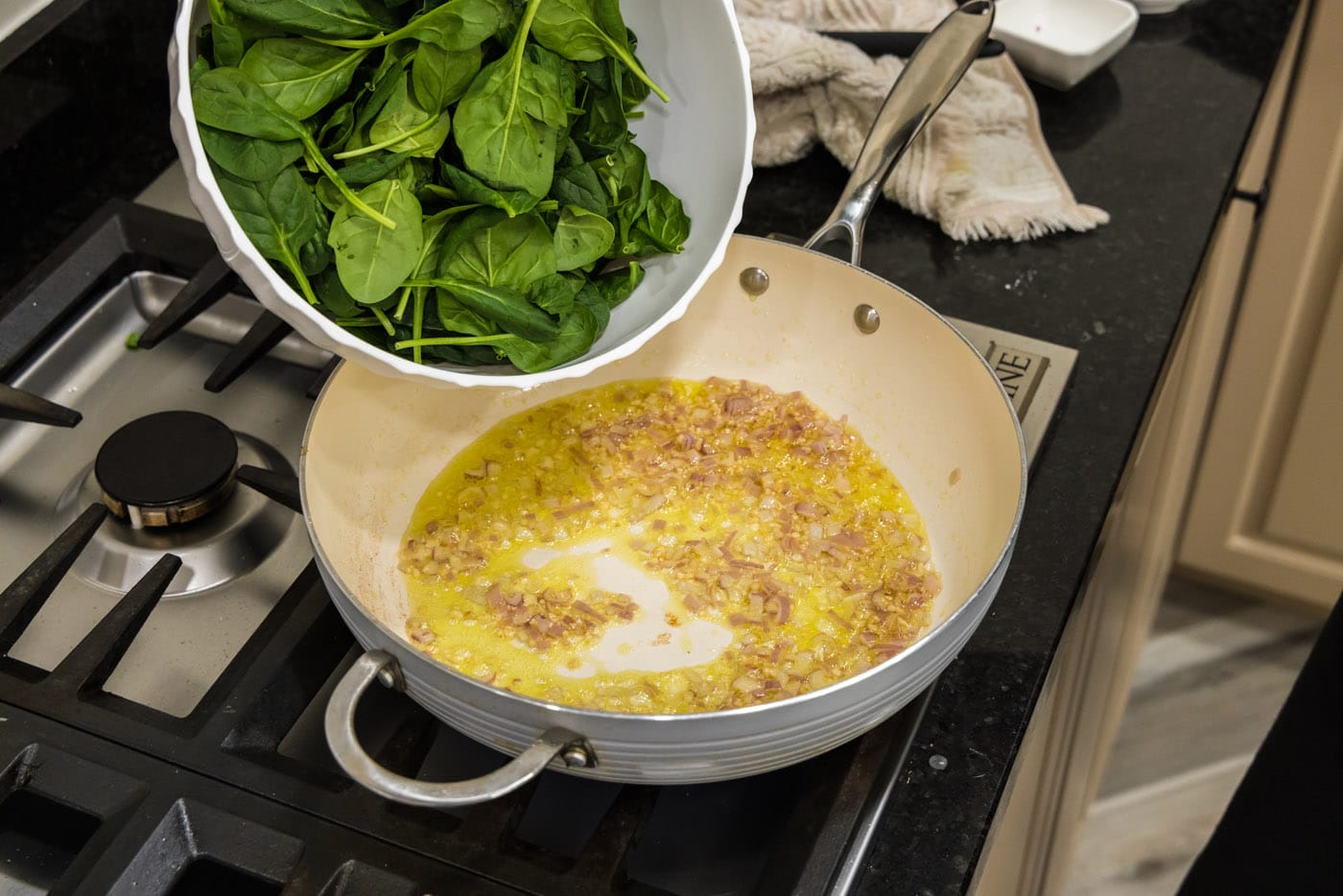 adding spinach to pan with shallots and garlic