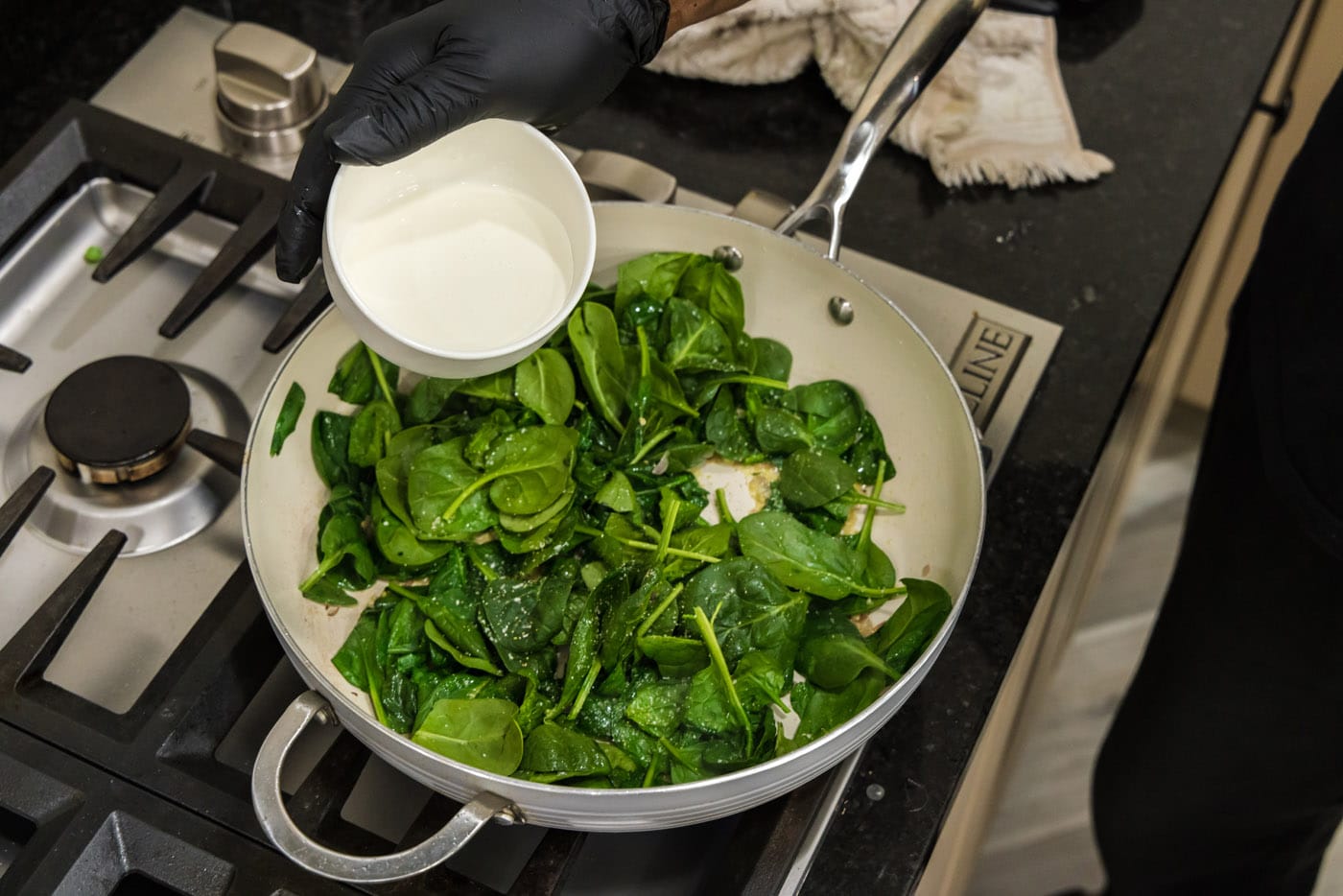 adding heavy cream to skillet with spinach, shallots, and garlic
