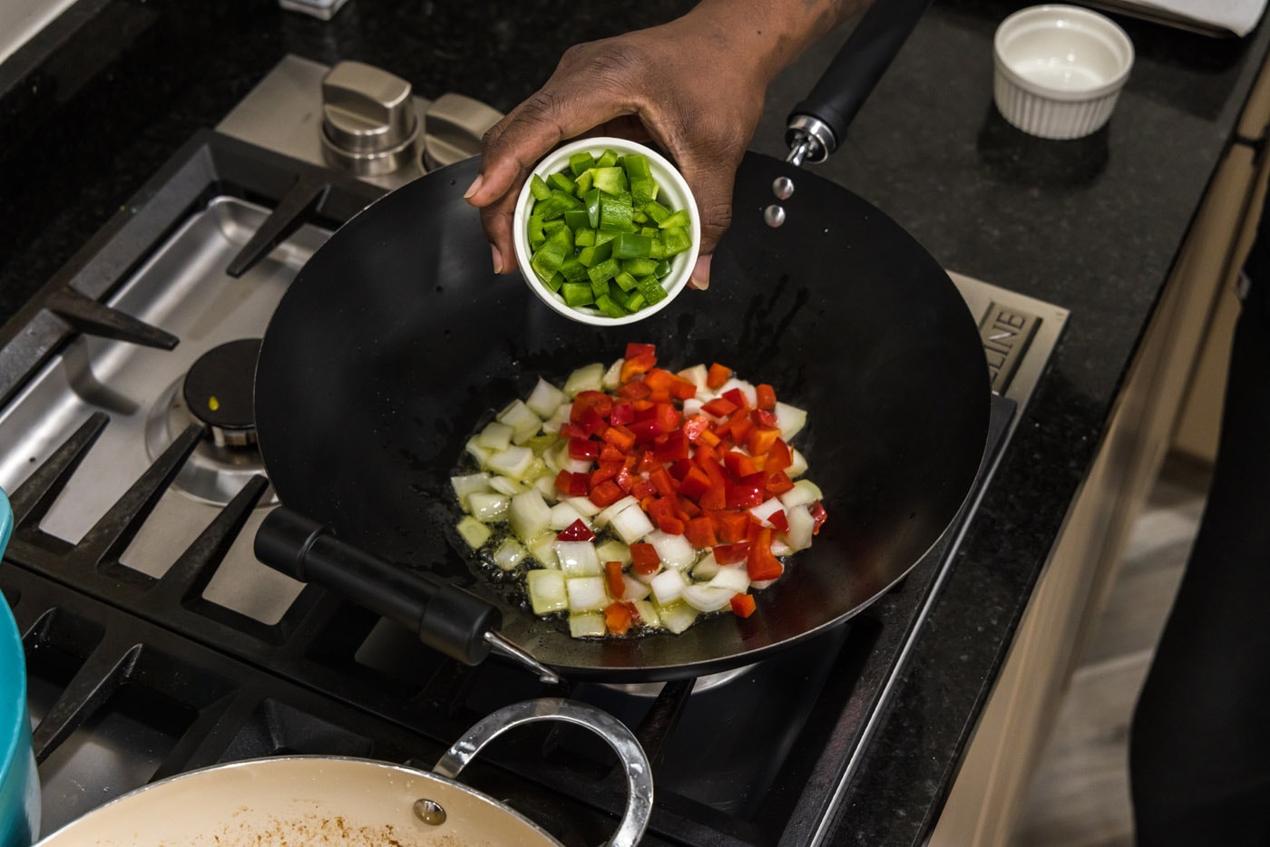 adding bell peppers and onions to a wok