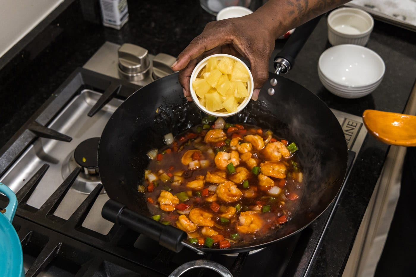 adding pineapple wedges to skillet of sweet and sour shrimp