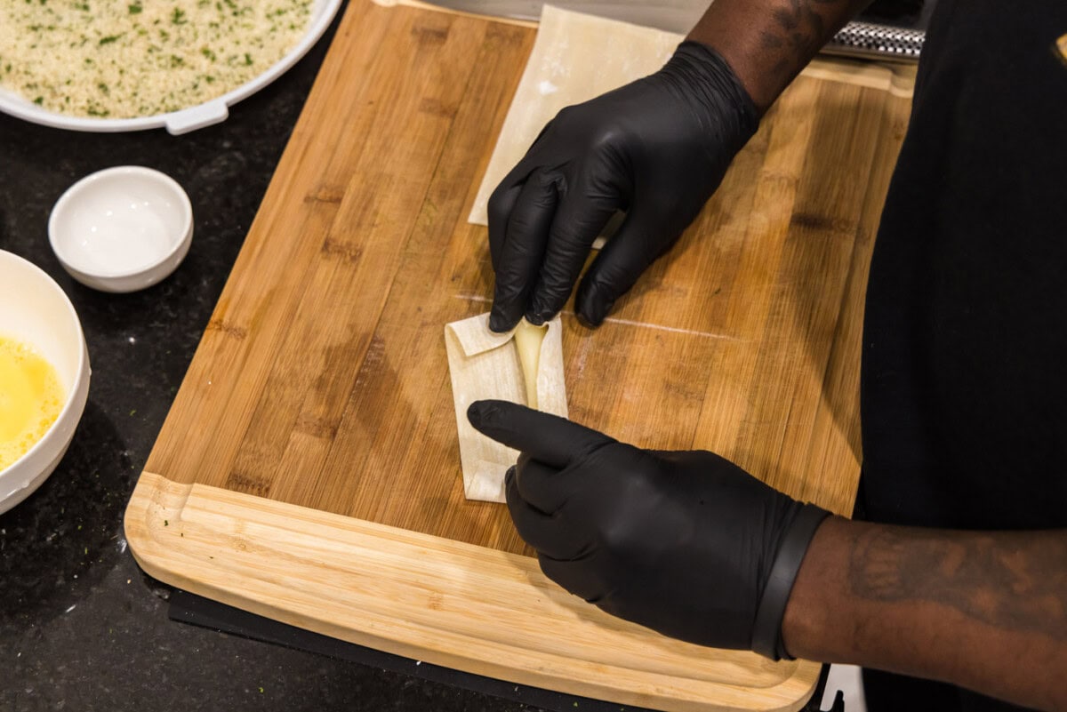 hands rolling a string cheese into an egg roll wrapper