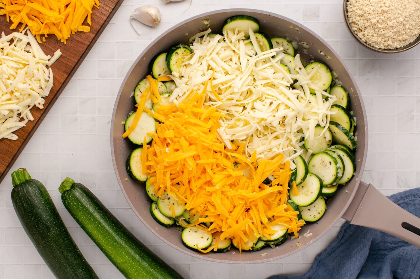 adding cheese to skillet with sliced zucchini
