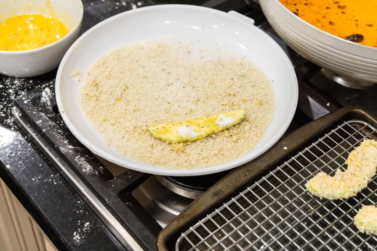 rolling flour dredged avocado slice in breadcrumbs